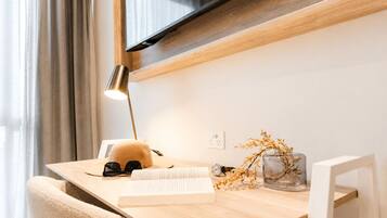 A wooden desk with a lamp, a book, a cap, and a vase with dried flowers.