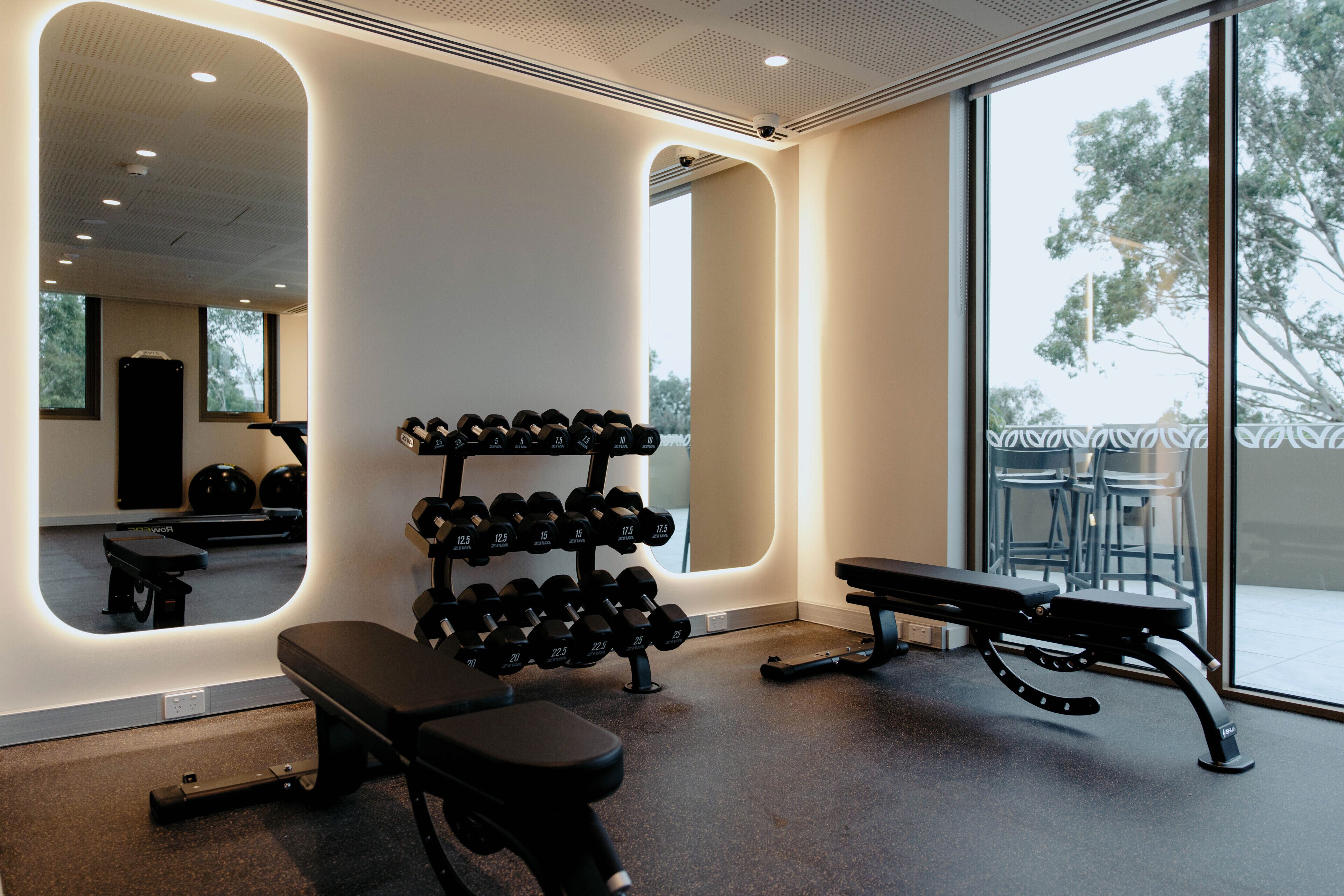 A gym with benches, dumbbells, and a large mirror.