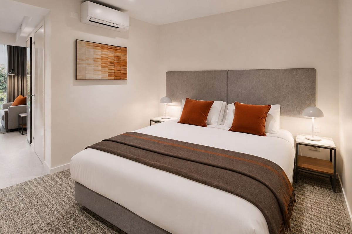 Moderni hotellihuone, jossa on suuri sänky, kaksi yöpöytää, seinään asennettu ilmastointilaite ja ovi, joka johtaa parvekkeelle.