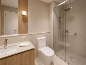 A modern bathroom with a glass-enclosed shower, a white toilet, a sink with a towel, and a wooden vanity. - Punthill Epping (Epping)