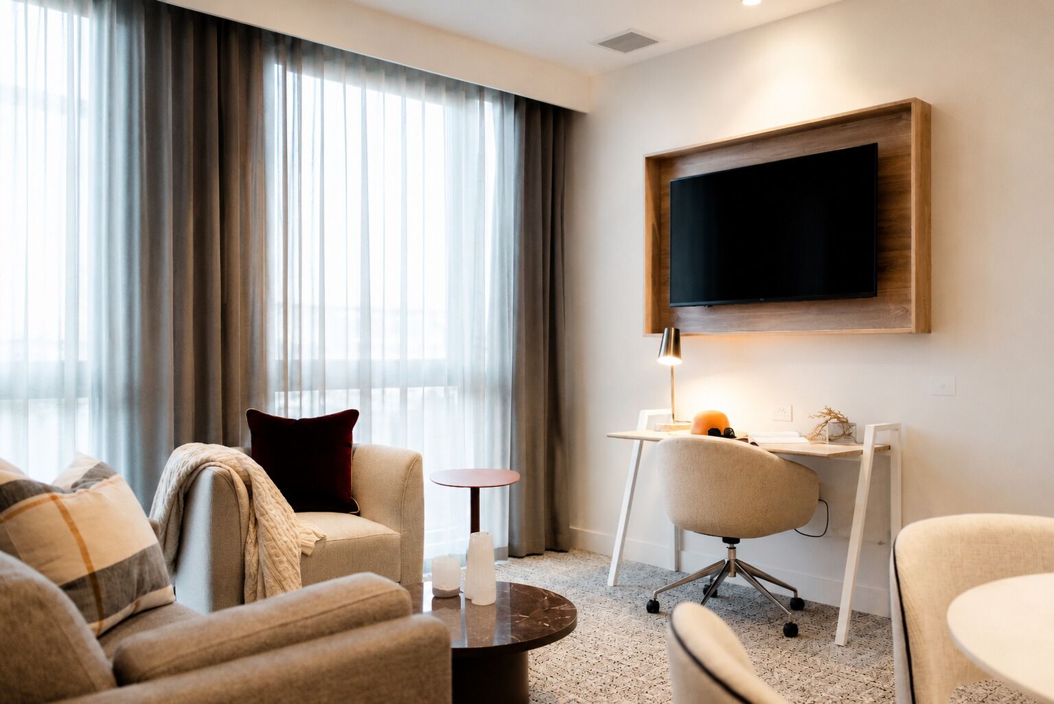 A hotel room with a sofa, armchair, desk, and TV.