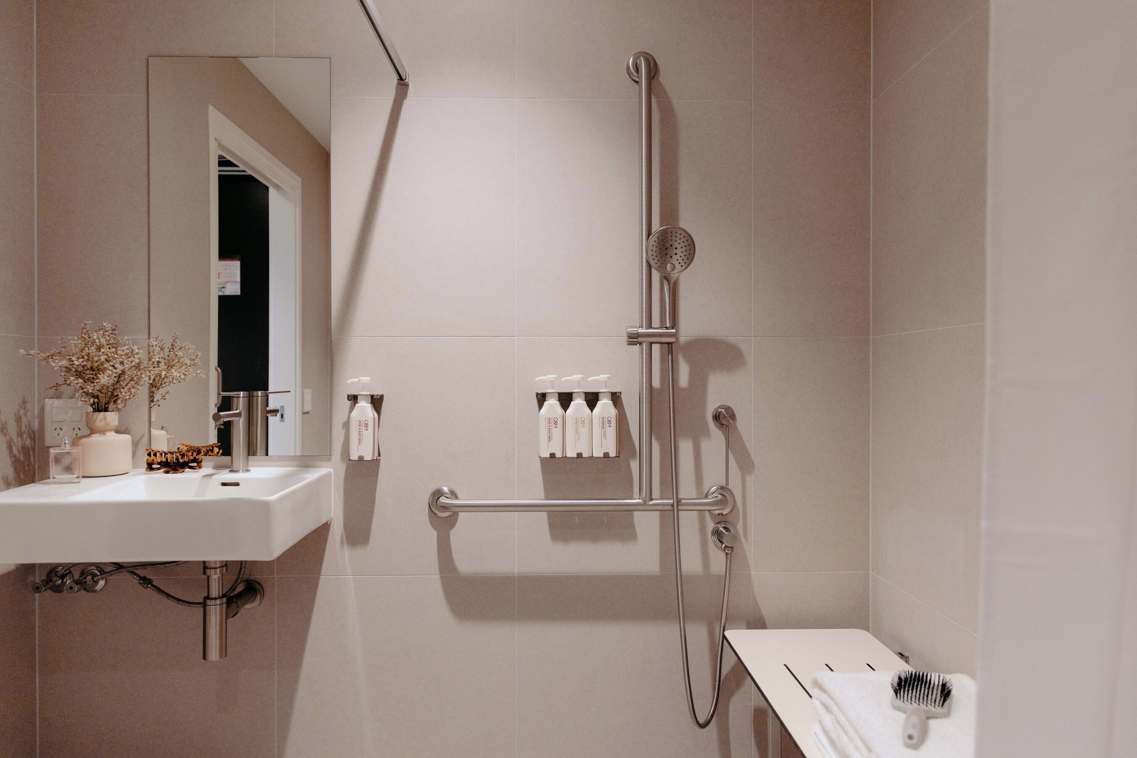 A modern bathroom with a sink, mirror, shower, and toiletries.