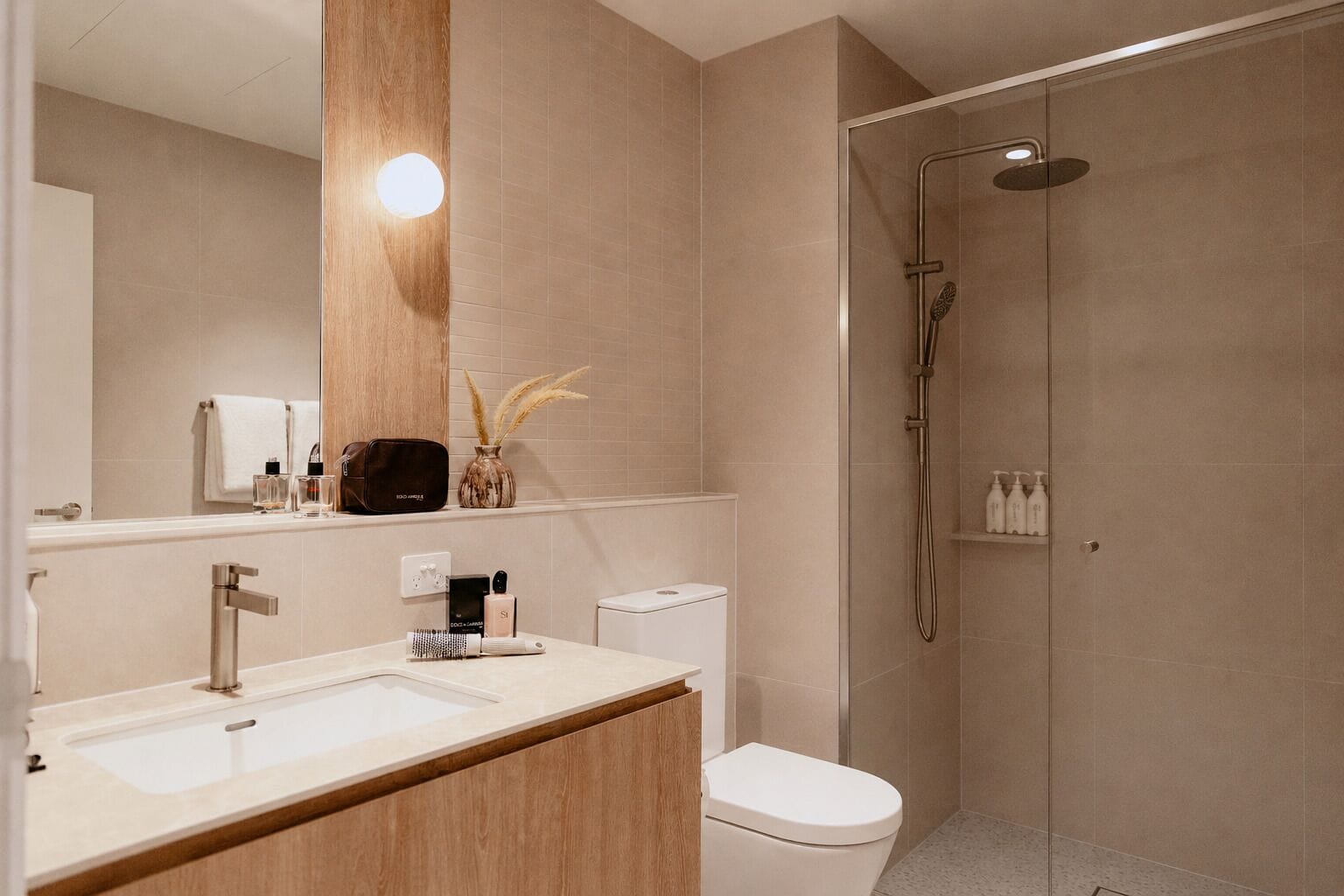 Un baño moderno con tocador de madera, inodoro, cabina de ducha y espejo con luz.