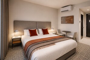 A hotel room with a large bed, two bedside tables, a chair, a small table, and an air conditioning unit on the wall. - Punthill Epping (Epping)