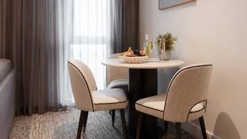 A dining area with a round table, two chairs, a vase with greenery, and a bottle of wine.