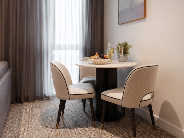 A dining area with a round table, two chairs, a vase with greenery, and a bottle of wine. - Punthill Epping (Epping)