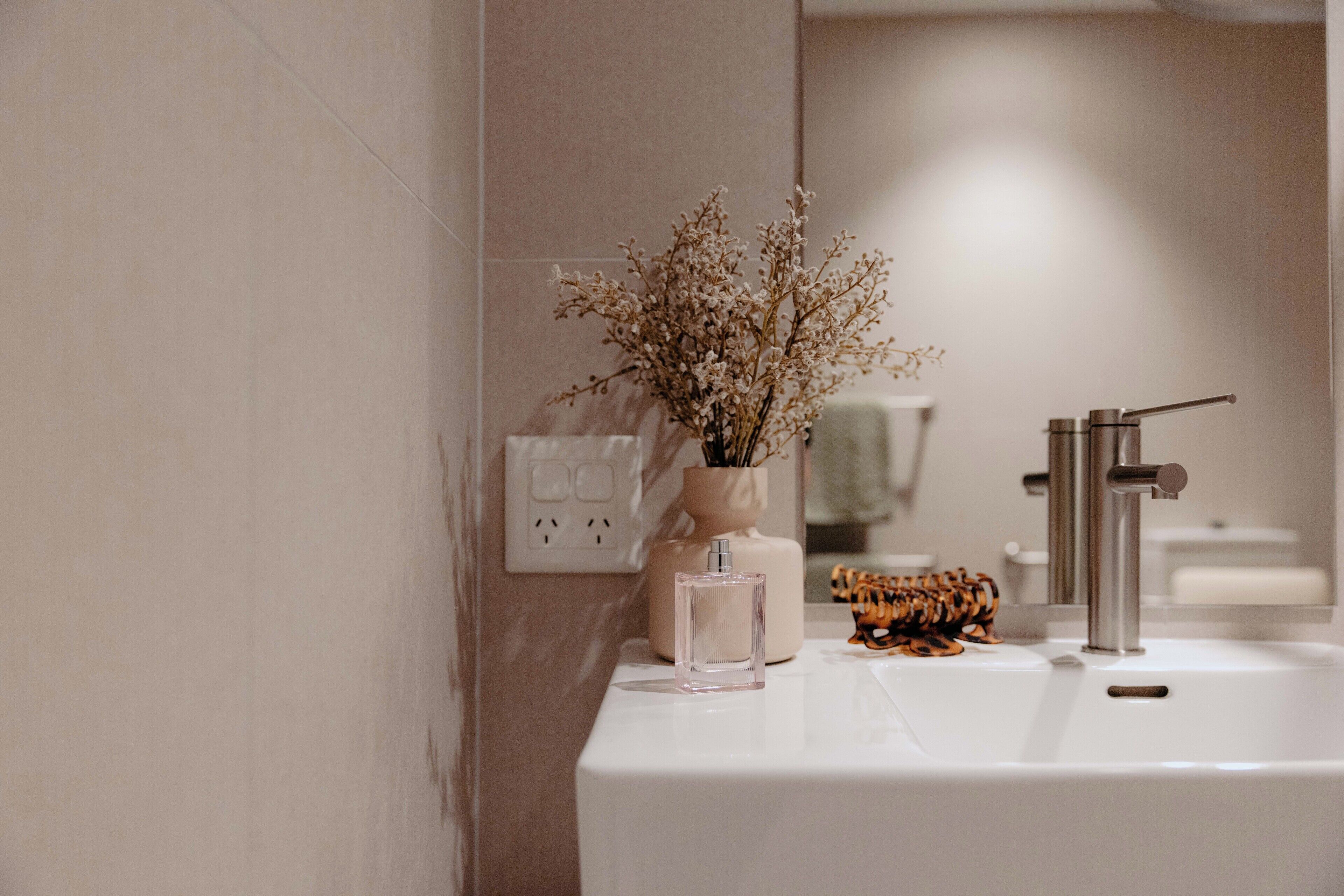 A bathroom with a white sink, a vase with dried flowers, and a mirror reflecting a towel.