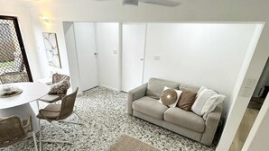 Una sala de estar moderna con un ventilador de techo blanco, un sofá gris con cojines estampados, una mesa de comedor con sillas y una alfombra de diseño en patrón de espiga.