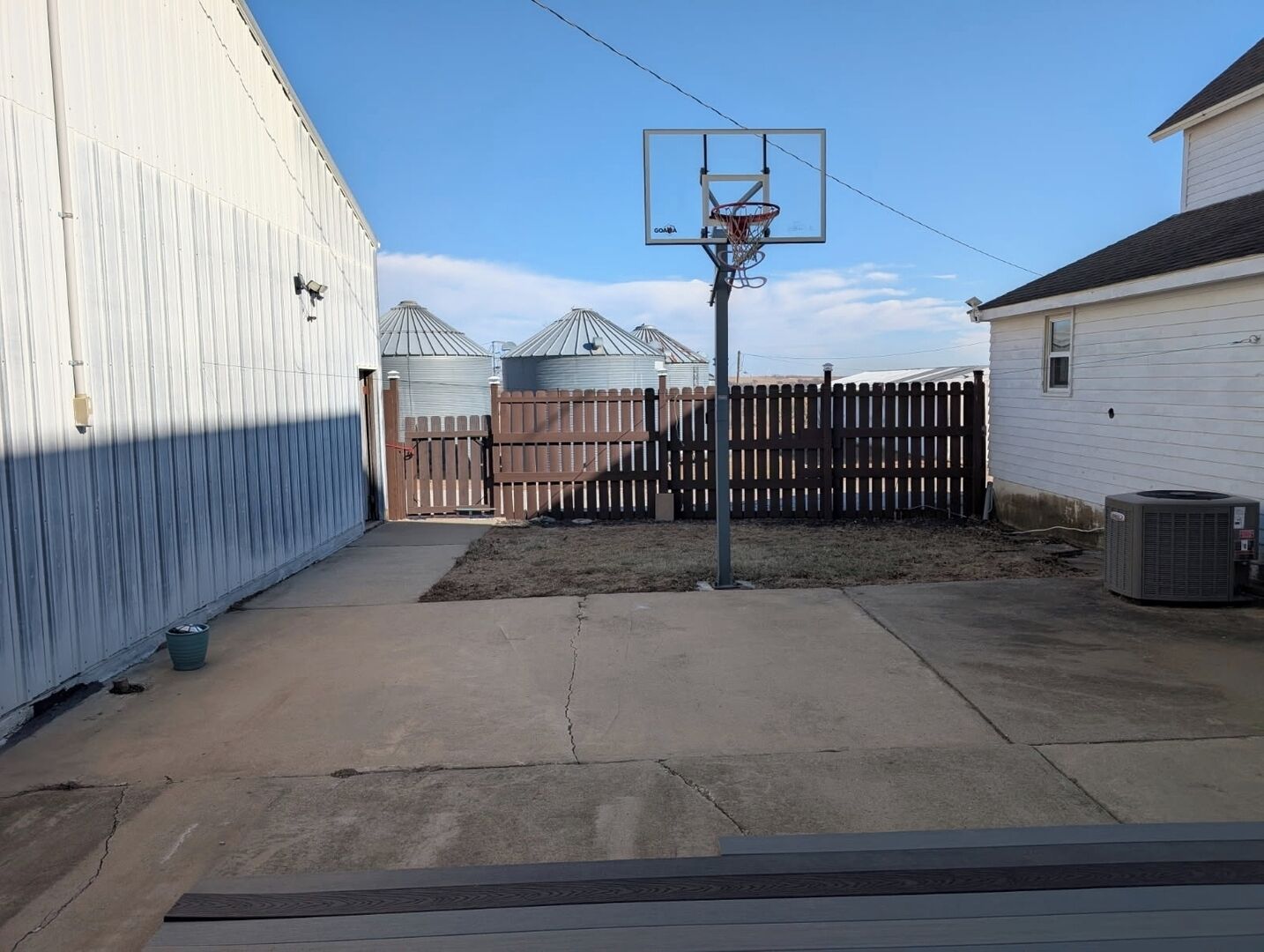 Un patio trasero con aro de baloncesto, valla de madera y una casa con techo de metal.