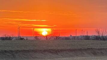 A sunset over a flat landscape with wind turbines in the distance.