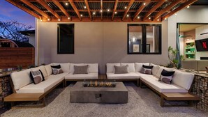 An outdoor living area with a sectional sofa, a fire pit, and a pergola with string lights. - Cactus Cove - Luxe Adventures by Hello Hideout (Austin)