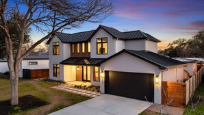 A modern two-story house with a garage, a well-maintained lawn, and a large tree in the front yard. - Cactus Cove - Luxe Adventures by Hello Hideout (Austin)
