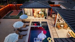 A backyard with a swimming pool, lounge chairs, umbrellas, and a basketball court. - Cactus Cove - Luxe Adventures by Hello Hideout (Austin)