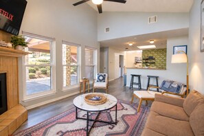 A spacious living room with a fireplace, a dining area with bar stools, and a kitchen in the background. - Dog-friendly condo with a gas fireplace, washer/dryer, AC, & cable TV (Canyon Lake)