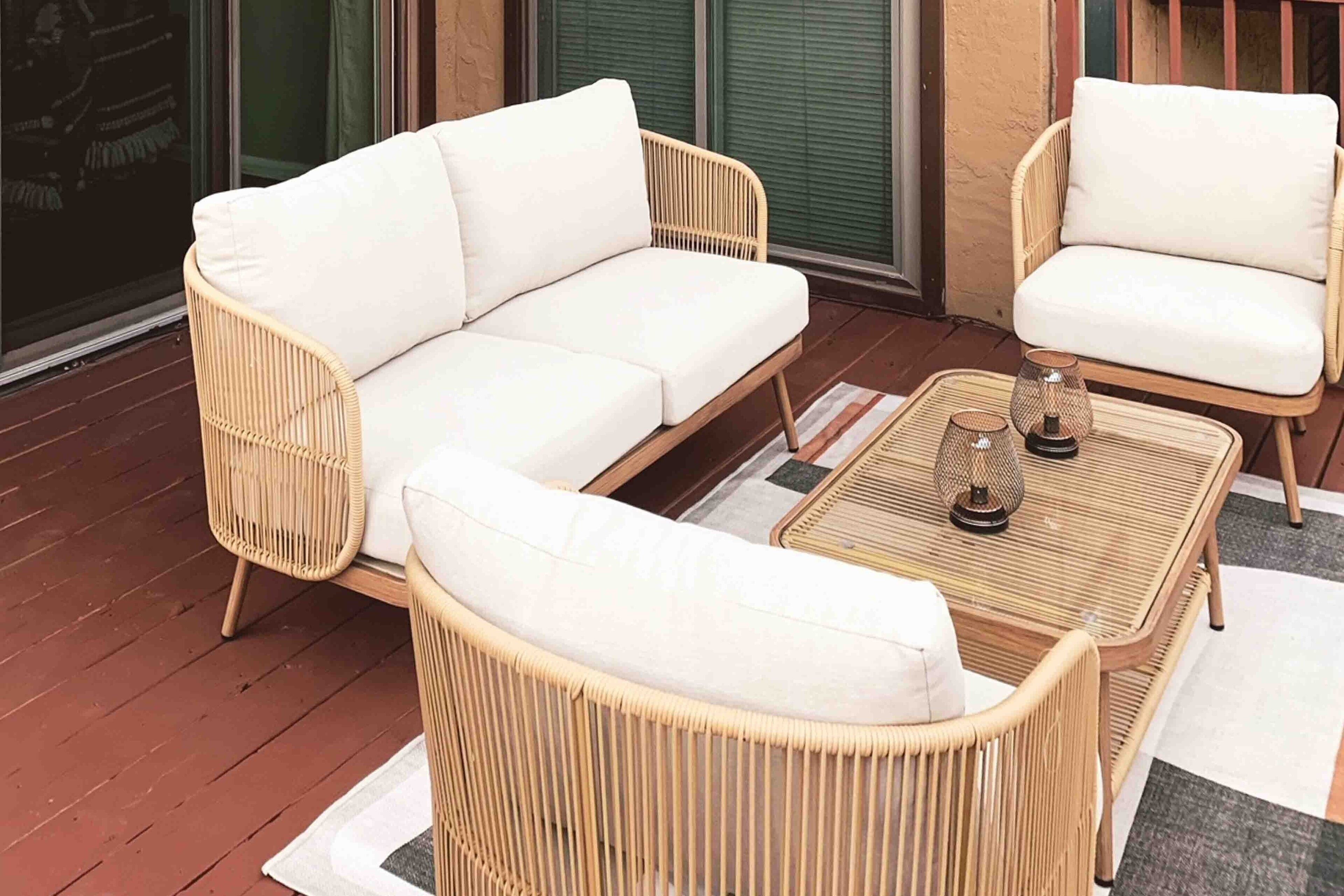 A wicker sofa and chair set on a wooden deck with a woven table and two glass candle holders.