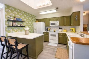A kitchen with green cabinets, a white refrigerator, a microwave, a stove, and a yellow toaster. There are two chairs with woven seats and black frames. - Dog-friendly condo with a gas fireplace, washer/dryer, AC, & cable TV (Canyon Lake)