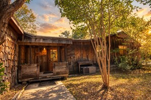 Un chalet rustique avec une façade en bois, une véranda dotée de sièges et un petit espace extérieur équipé d’un barbecue.