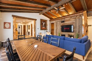 Un salon moderne avec une table à manger en bois, un canapé bleu et un téléviseur fixé au mur.
