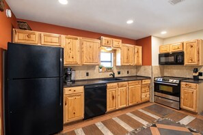 A kitchen with wooden cabinets, a black refrigerator, a dishwasher, a microwave, and an oven. - Newly renovated rustic home with deck by Horseshoe and Tubing (Canyon Lake)