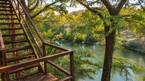 Un pont en bois, doté d’une rambarde métallique, surplombe une rivière bordée d’arbres.