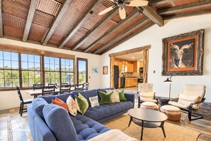 A spacious living area with a large blue sofa, a dining table, and chairs. There is a kitchen visible through an open doorway. - Newly renovated rustic home with deck by Horseshoe and Tubing (Canyon Lake)
