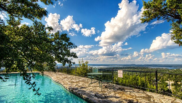 Una piscina con baldosas de piedra, una valla de metal y vistas del paisaje.