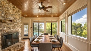 Un comedor con chimenea de piedra, techo de madera y grandes ventanales con vista a árboles.