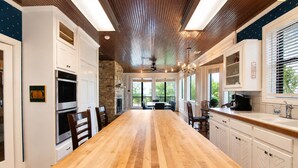 Una cocina amplia con una larga mesa de madera, armarios blancos y una pared de acento de piedra.