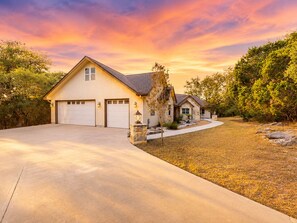 A two-story house with a garage, a stone entrance, and a driveway leading to the front door. - 5-acre Hill Country home with views & outdoor entertaining - dog-friendly (Canyon Lake)