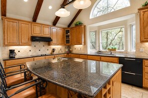 A kitchen with wooden cabinets, a granite countertop, a black dishwasher, and a large window with a view of trees. - 5-acre Hill Country home with views & outdoor entertaining - dog-friendly (Canyon Lake)