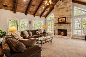 A spacious living room with a stone fireplace, wooden ceiling beams, and large windows. - 5-acre Hill Country home with views & outdoor entertaining - dog-friendly (Canyon Lake)