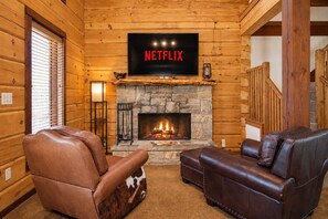 A log cabin interior with a stone fireplace, leather sofas, and a television mounted above the fireplace displaying 'NETFLIX'. - Luxe Lake Living with Bonus Bunk Area & Private Boat Parking - Dogs Welcome (Canyon Lake)