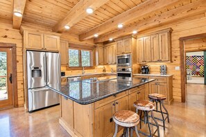 A kitchen with wooden cabinets, stainless steel appliances, a large island with stools, and a view of the outdoors. - Luxe Lake Living with Bonus Bunk Area & Private Boat Parking - Dogs Welcome (Canyon Lake)