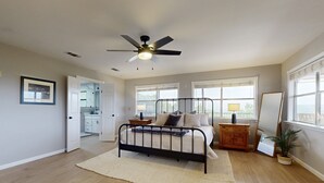 Ein Schlafzimmer mit einem Bett, einem Deckenventilator, einem Nachttisch, einer Lampe und einer Topfpflanze.
