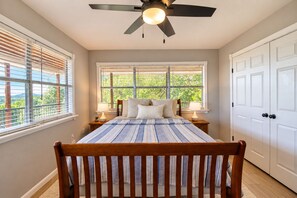 A bedroom with a bed, two bedside tables, a ceiling fan, and a view of greenery through the windows. - Spacious house with living room, kitchen, balcony and Hill country views (Canyon Lake)