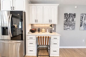 A modern kitchen with white cabinetry, a stainless steel refrigerator, a bar stool, and a countertop with a water dispenser. - Spacious house with living room, kitchen, balcony and Hill country views (Canyon Lake)