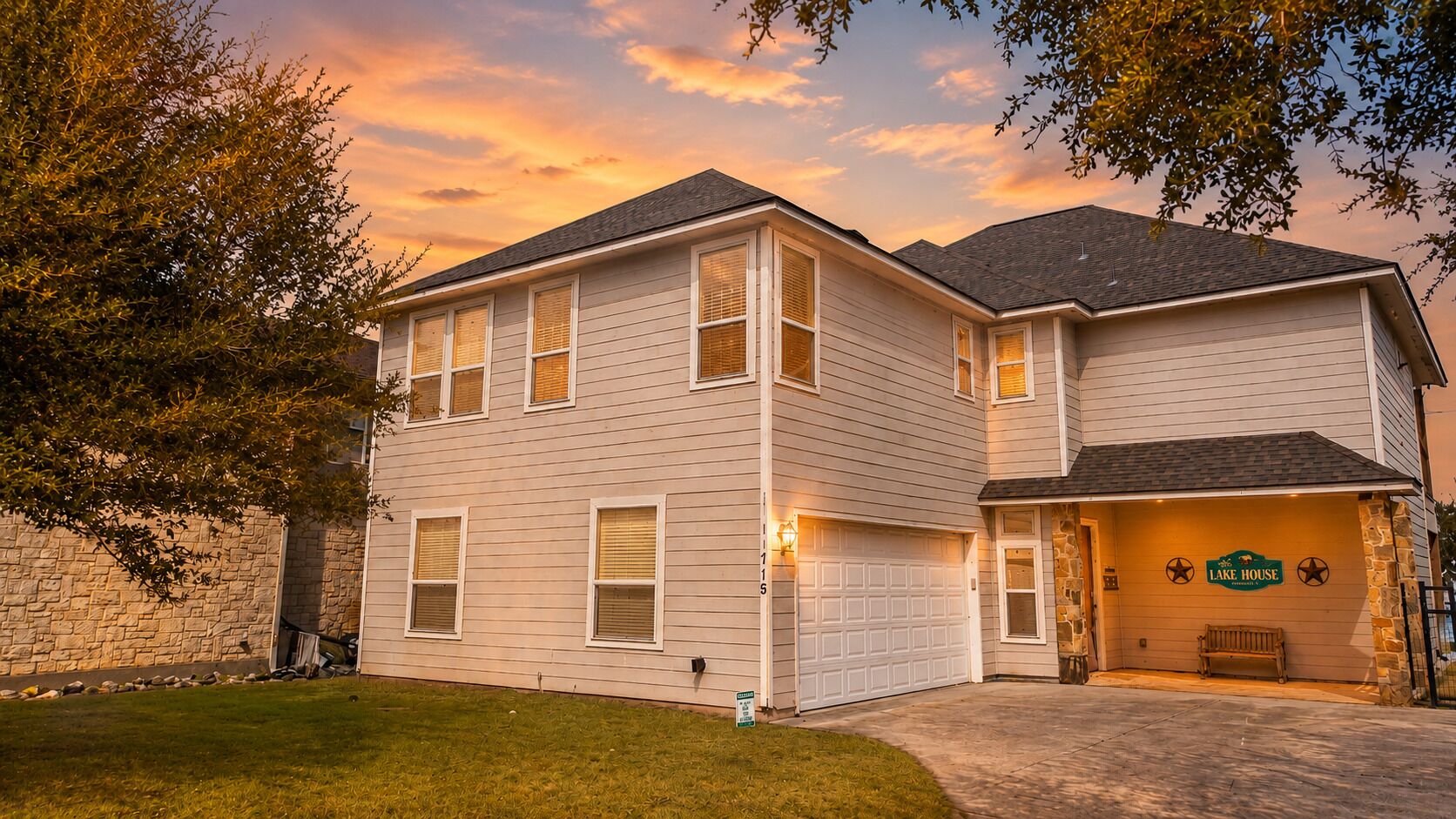 A two-story house with a garage, a stone wall, and a well-maintained lawn.