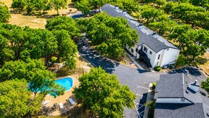Vista aérea de una zona residencial con piscina, árboles y una casa con techo inclinado.