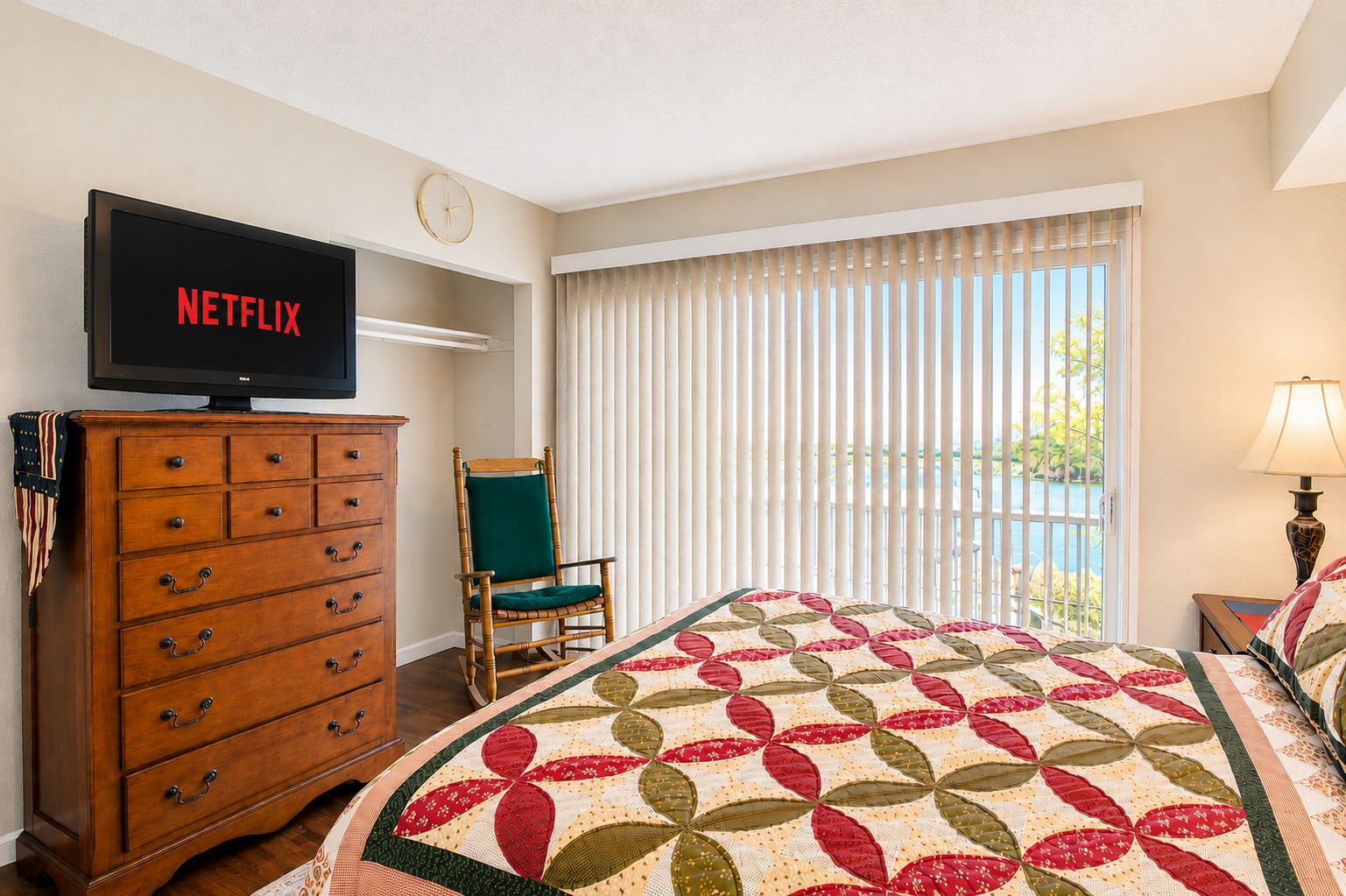 Ett hotellrum med en säng, en byrå i trä, en tv som visar ”NETFLIX”, en stol och ett fönster med persienner.