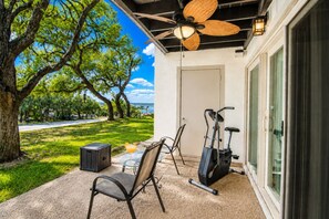 An outdoor patio with a ceiling fan, exercise equipment, a table with chairs, and a glass door leading to a covered area.