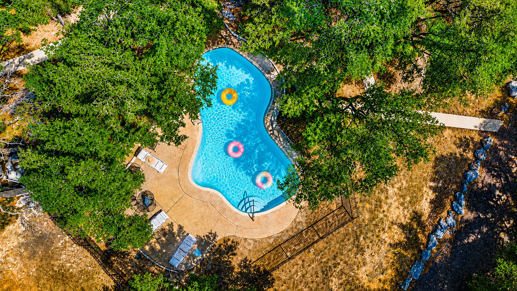 Vista aérea de una piscina rodeada de árboles, con algunas sillas de descanso y una pequeña zona de terraza.