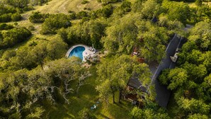 Vista aérea de una propiedad con piscina rodeada de exuberante vegetación, un edificio de estilo tradicional y un techo curvo.