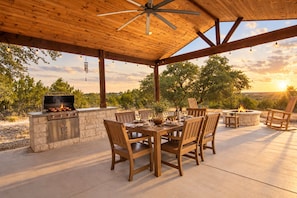 An outdoor patio with a stone barbecue, wooden dining table, chairs, and a fire pit. - Lovely home on 2+ acres with views, firepit & outdoor kitchen - wedding perfect (Dripping Springs)