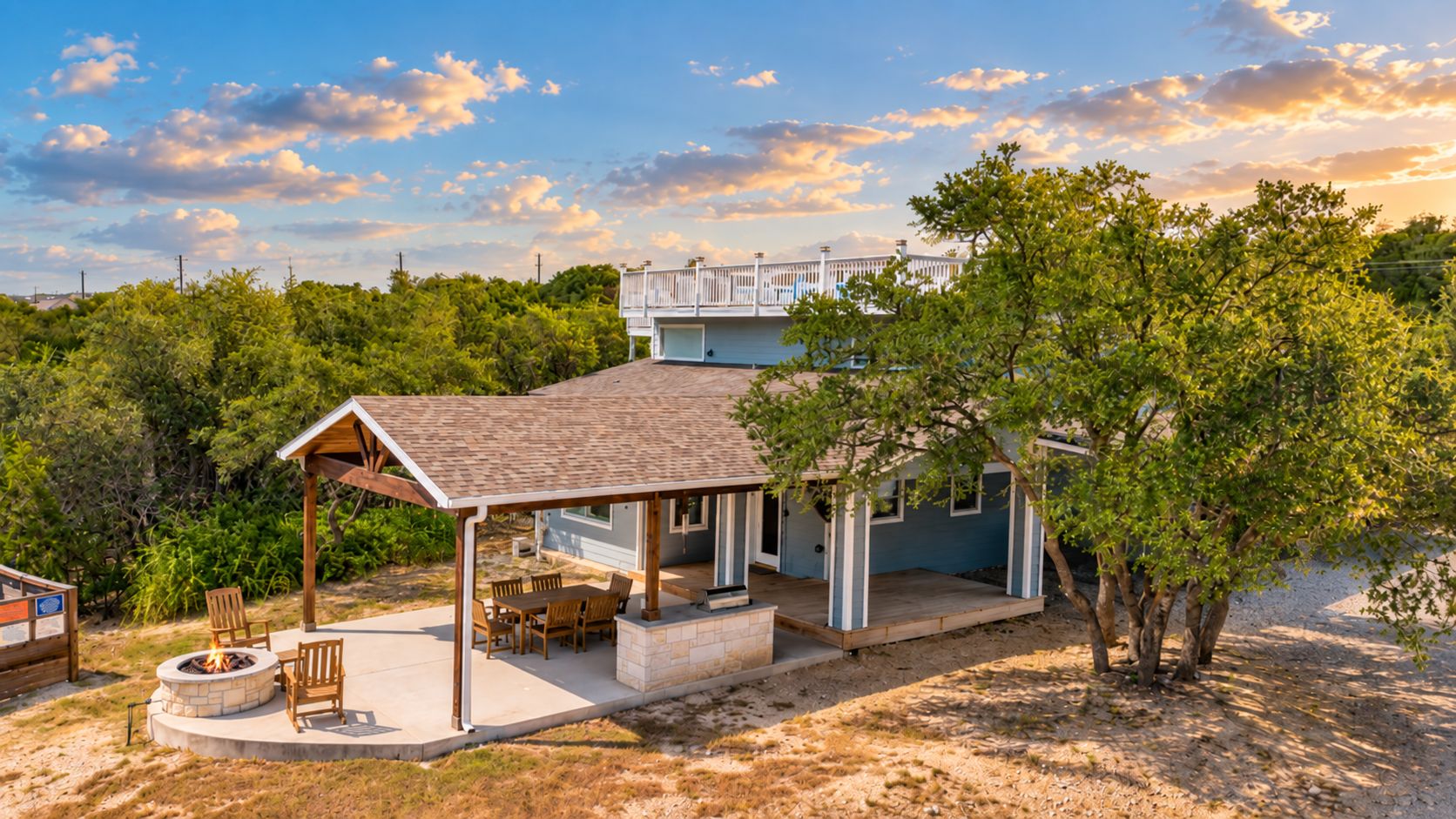 A two-story house with a covered patio, a fire pit, and a view of a bridge in the background.