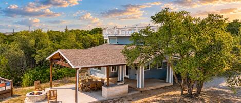A two-story house with a covered patio, a fire pit, and a view of a bridge in the background.