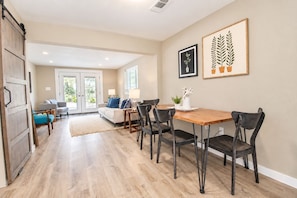 A spacious living area with a dining table, chairs, and a sofa. There is a sliding door leading to a balcony. - Lovely home on 2+ acres with views, firepit & outdoor kitchen - wedding perfect (Dripping Springs)