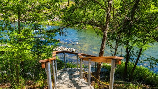 Una escalera de piedra que conduce a una plataforma de madera con vistas a un lago, rodeada de árboles.