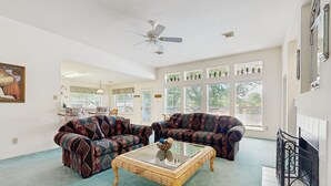 Una sala de estar con sofás estampados, una mesa de centro de cristal y un ventilador de techo.