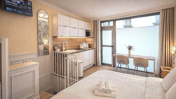 Hotelkamer met een bed, een kleine kitchenette, een eethoek met tafel en stoelen, en een groot raam met uitzicht.