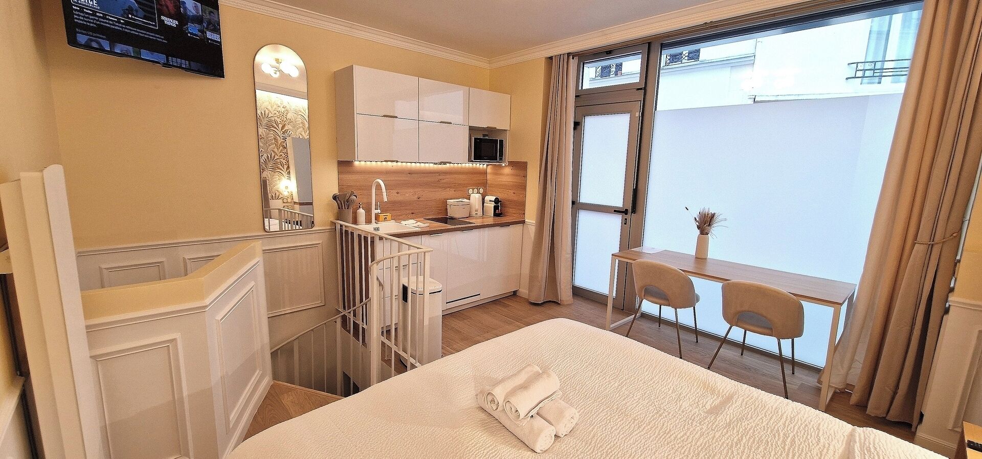 A hotel room with a bed, a small kitchenette, a dining area, and a view of the city.